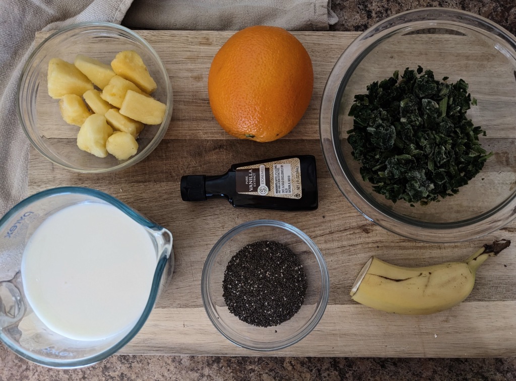 Wholesome ingredients for dreamy orange smoothie, including frozen pineapple, fresh orange, fresh banana, frozen spinach, milk, vanilla extract, and chia seeds